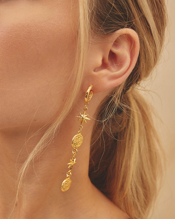 Primer plano de oreja de mujer luciendo los Maxi Aretes Cassiopeia con dijes de estrellas y dijes martillados